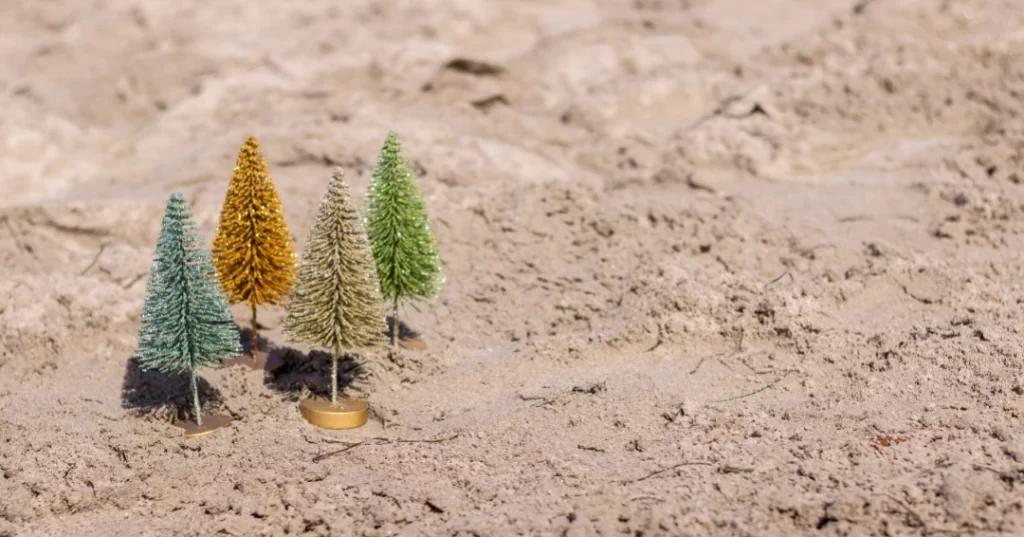 four miniature christmas trees in the sand.